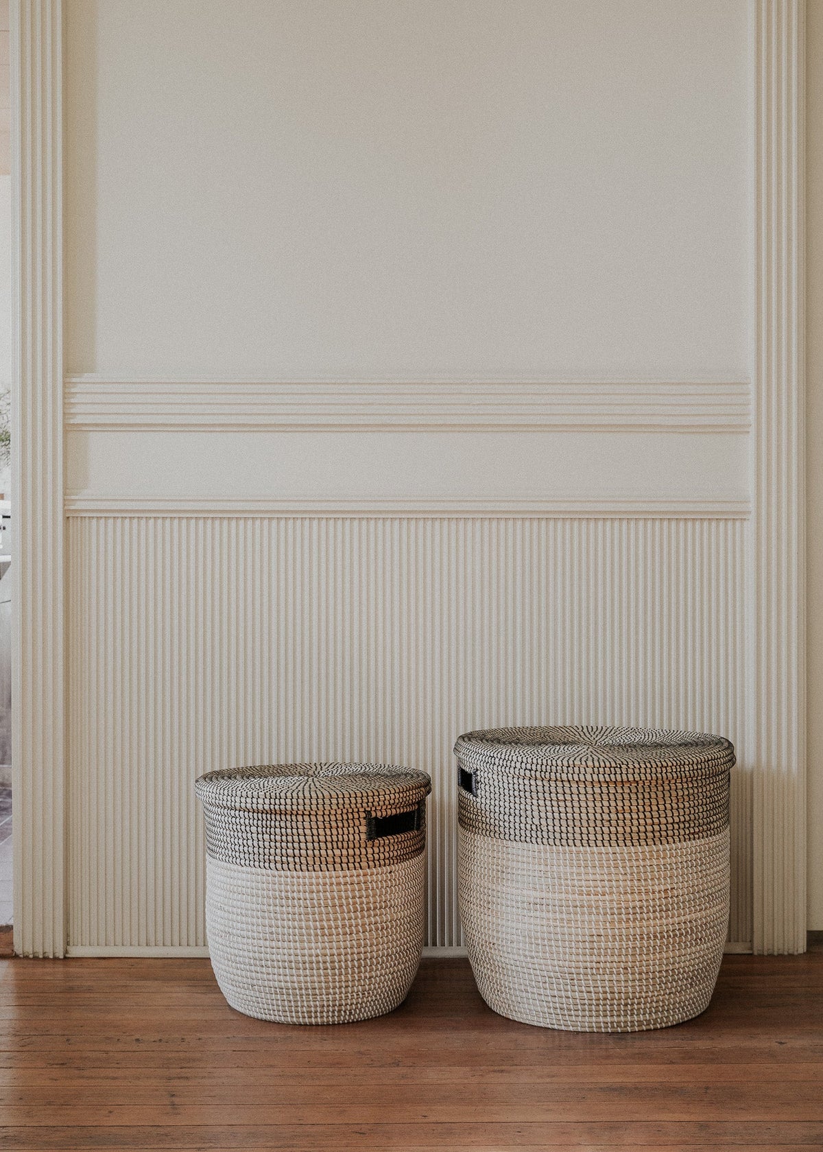 Two Black Medina baskets displayed beneath decorative wall molding in a minimal interior.