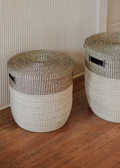 Two lidded Black Medina baskets styled on a wood floor in a paneled room.