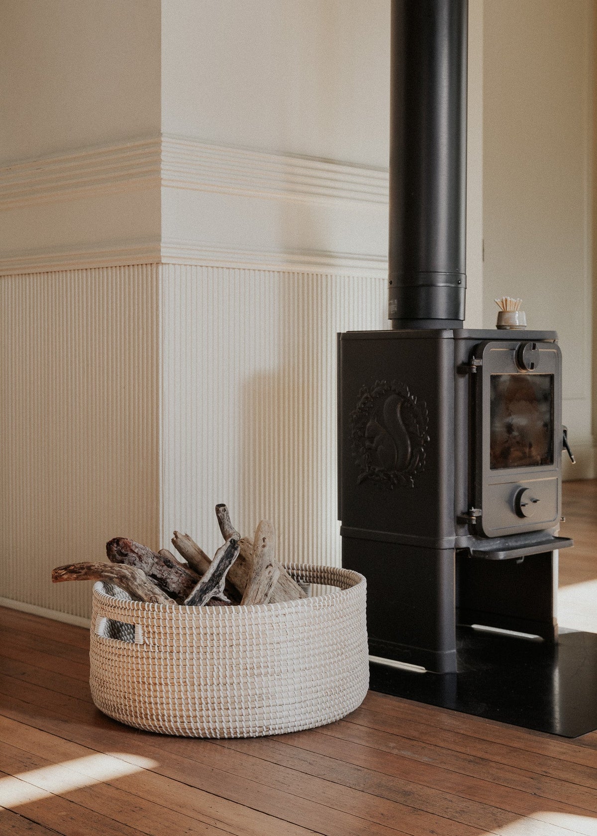 Medina floor basket filled with firewood beside a black wood-burning stove.