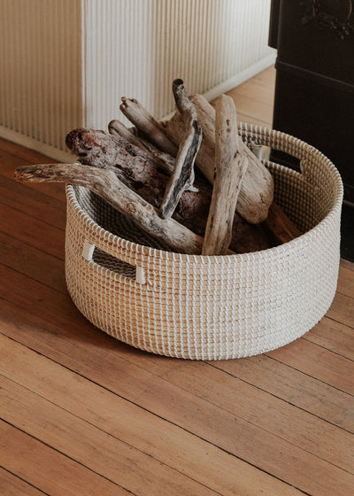 Close view of the seagrass basket holding split logs on a warm wood floor.