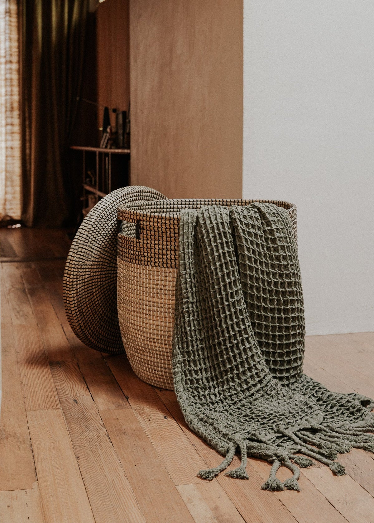 Large Black Medina basket in a wood-floored hallway with a textured green throw draped over it.