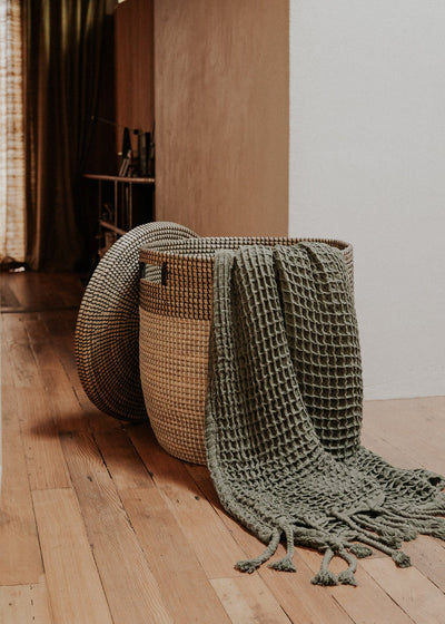 Large Black Medina basket in a wood-floored hallway with a textured green throw draped over it.
