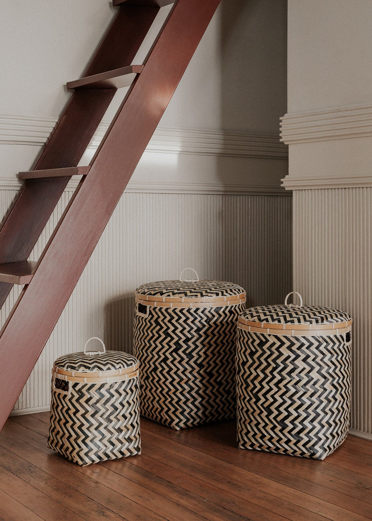 Three Java baskets arranged beneath a wooden staircase on a dark wood floor.
