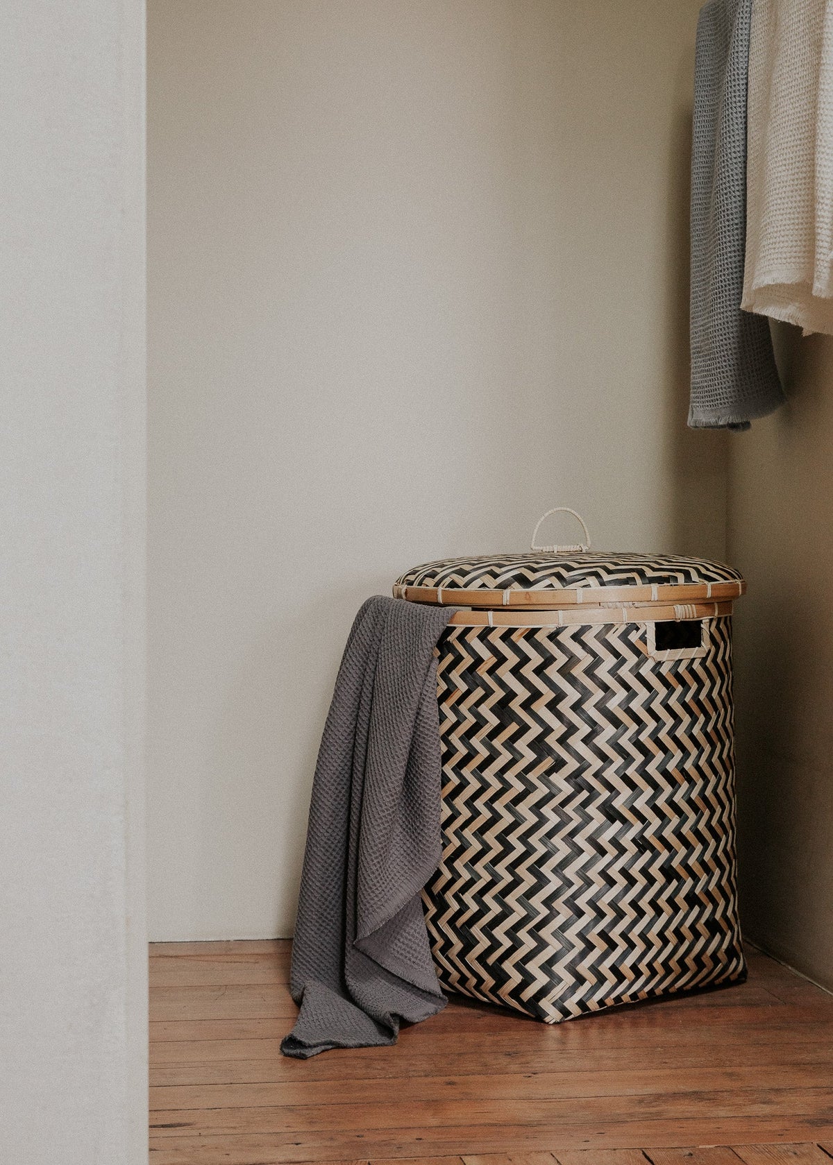 Large lidded Java basket styled in a room corner with a gray textile draped beside it.