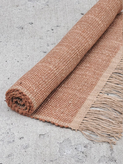 Korissa Goldilocks Rug, brown colorway, rolled up on concrete floor