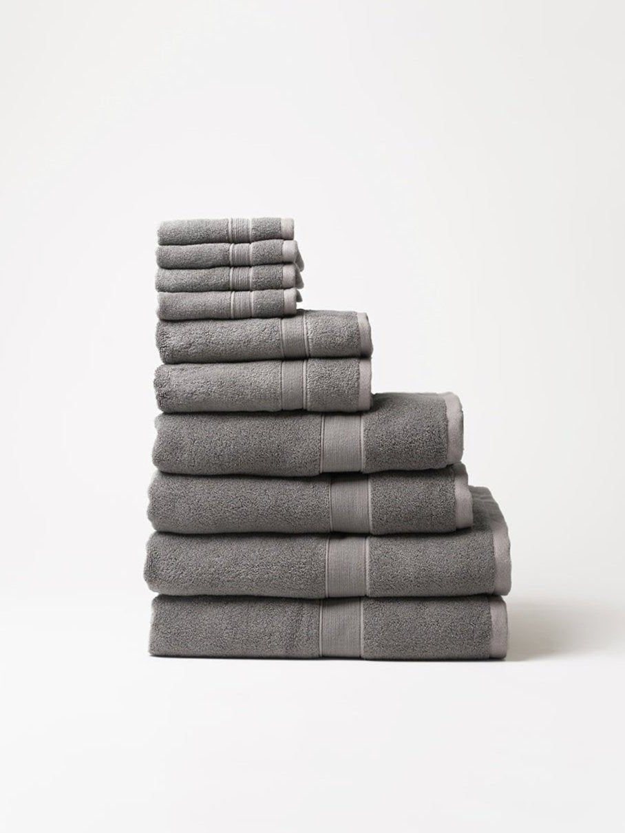 Charcoal gray towels stacked in a stepped arrangement on a pale background, showing plush fabric, thick folded edges, and matching woven border bands.
