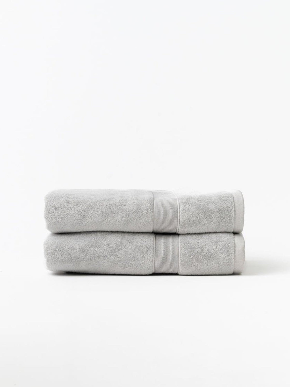 Two light gray bath towels stacked on a white background, showing thick folded edges and matching woven border bands.