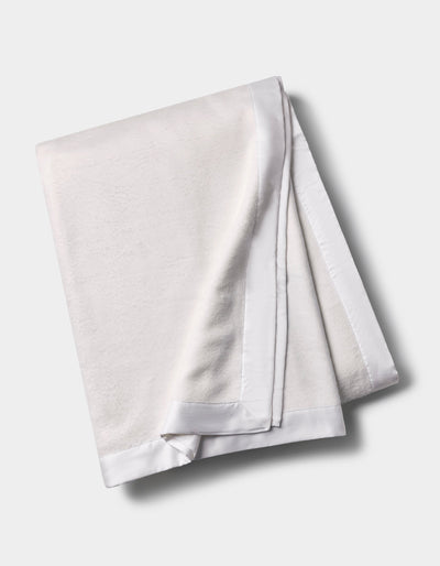 White Bamboo Blanket folded lengthwise on a pale background, showing its subtle texture and smooth white satin edging.