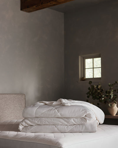 White Bamboo Viscose Comforter folded on a pale background, with one corner turned back to show its quilted surface, softly padded layers, and finished edge.