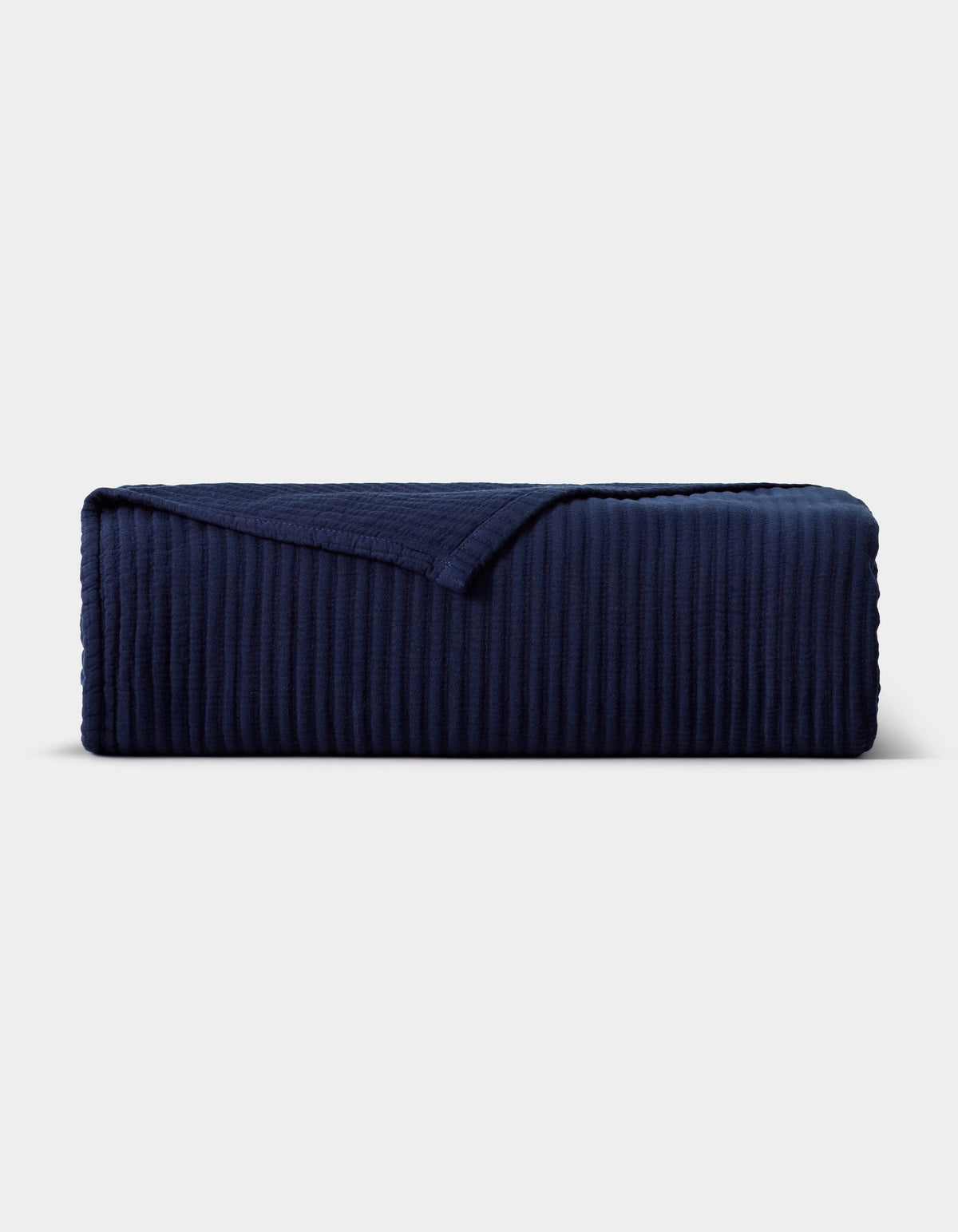 Navy blue Bamboo Coverlet folded into a rectangular stack on a pale background, with raised vertical ribs and one corner turned back.