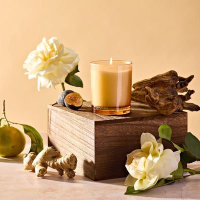 APOTHEKE Cedarwood Ginger Petite Candle styled on a wood block with white flowers, ginger root, and a pear