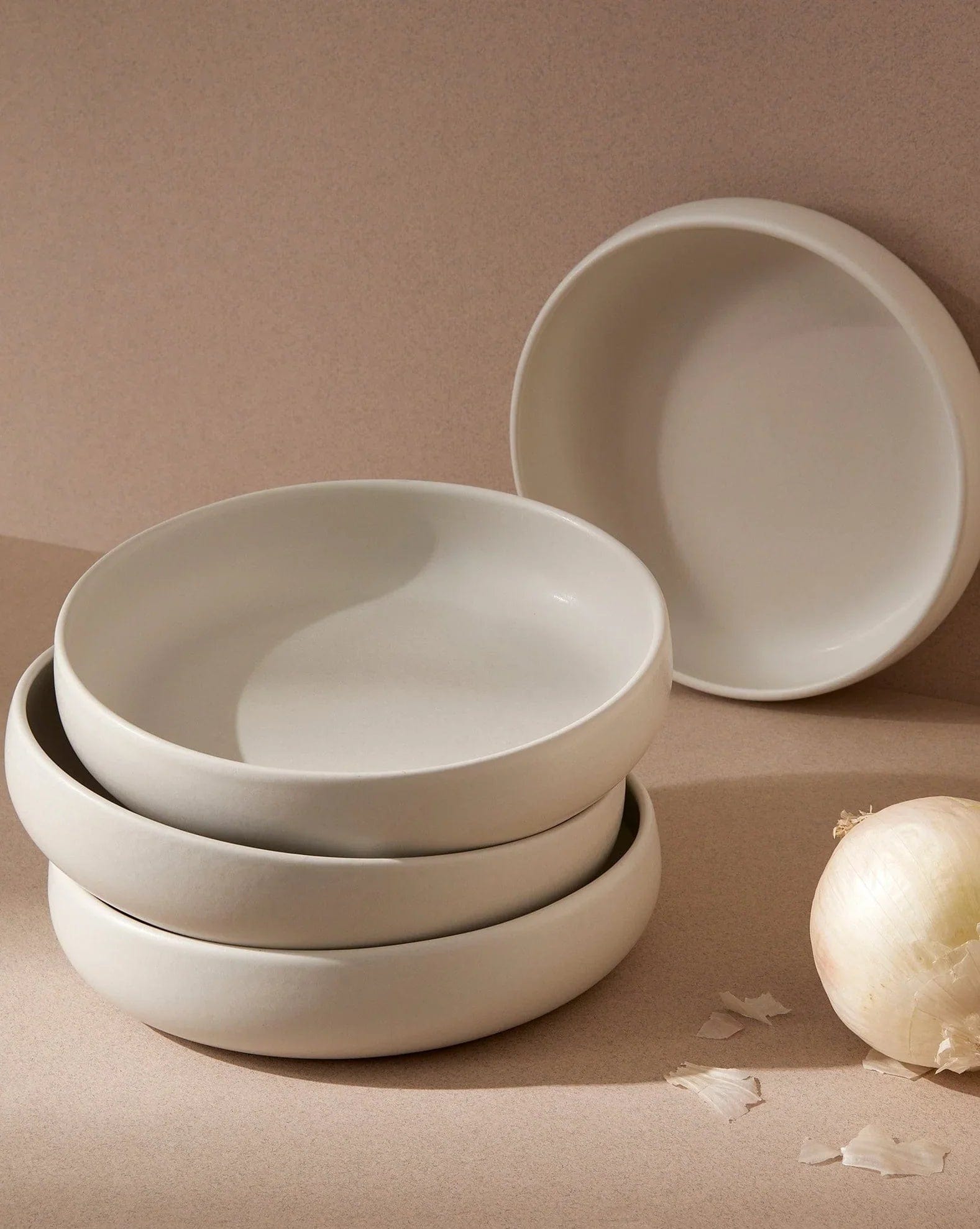 Stoneware pasta bowls in Matte White stacked with onion on neutral background