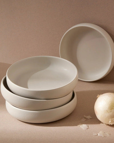 Stoneware pasta bowls in Matte White stacked with onion on neutral background
