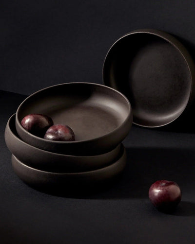 Stoneware pasta bowls in Matte Black stacked with plums on dark background