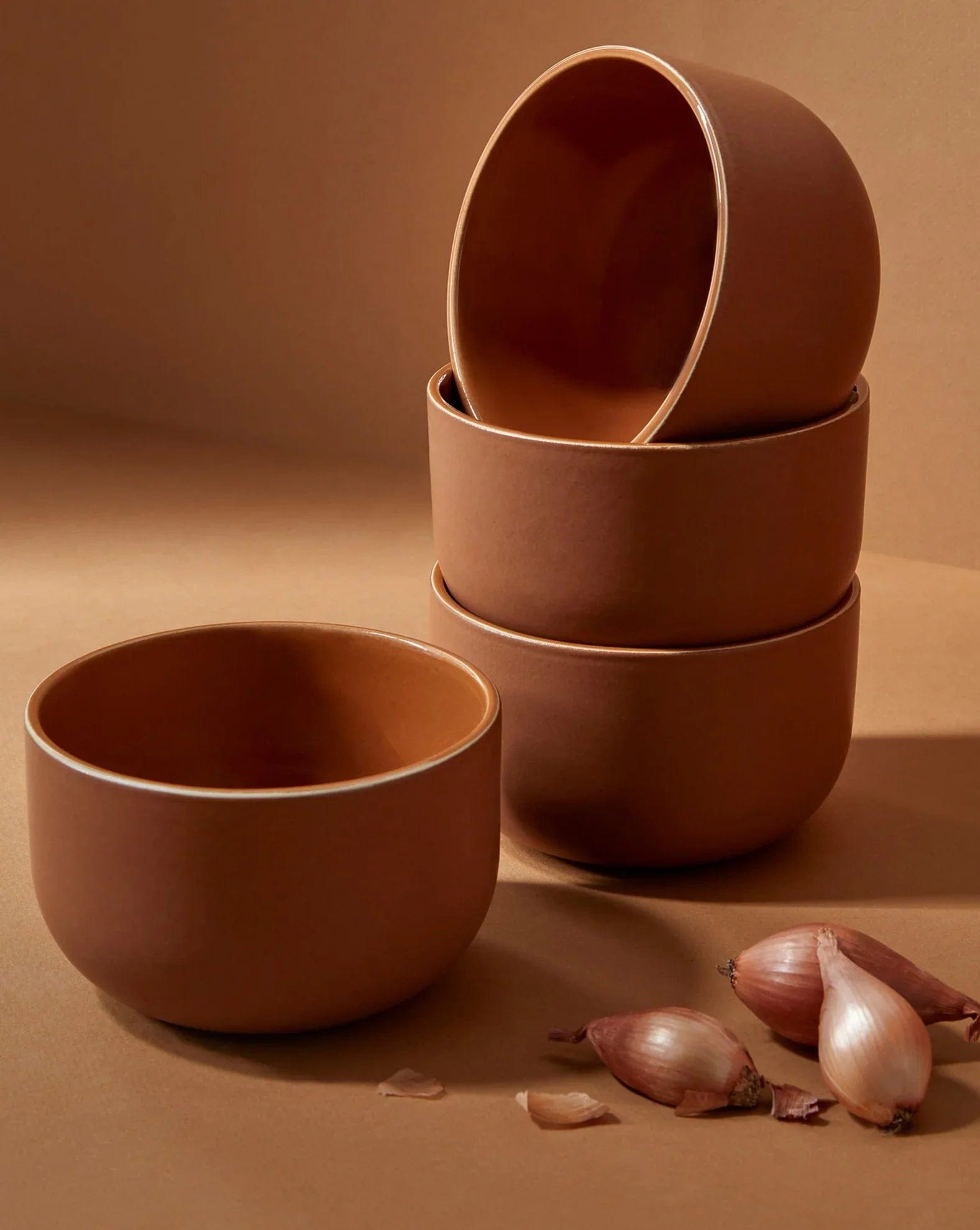 Stoneware bowls in Terracotta stacked with shallots on warm-toned background
