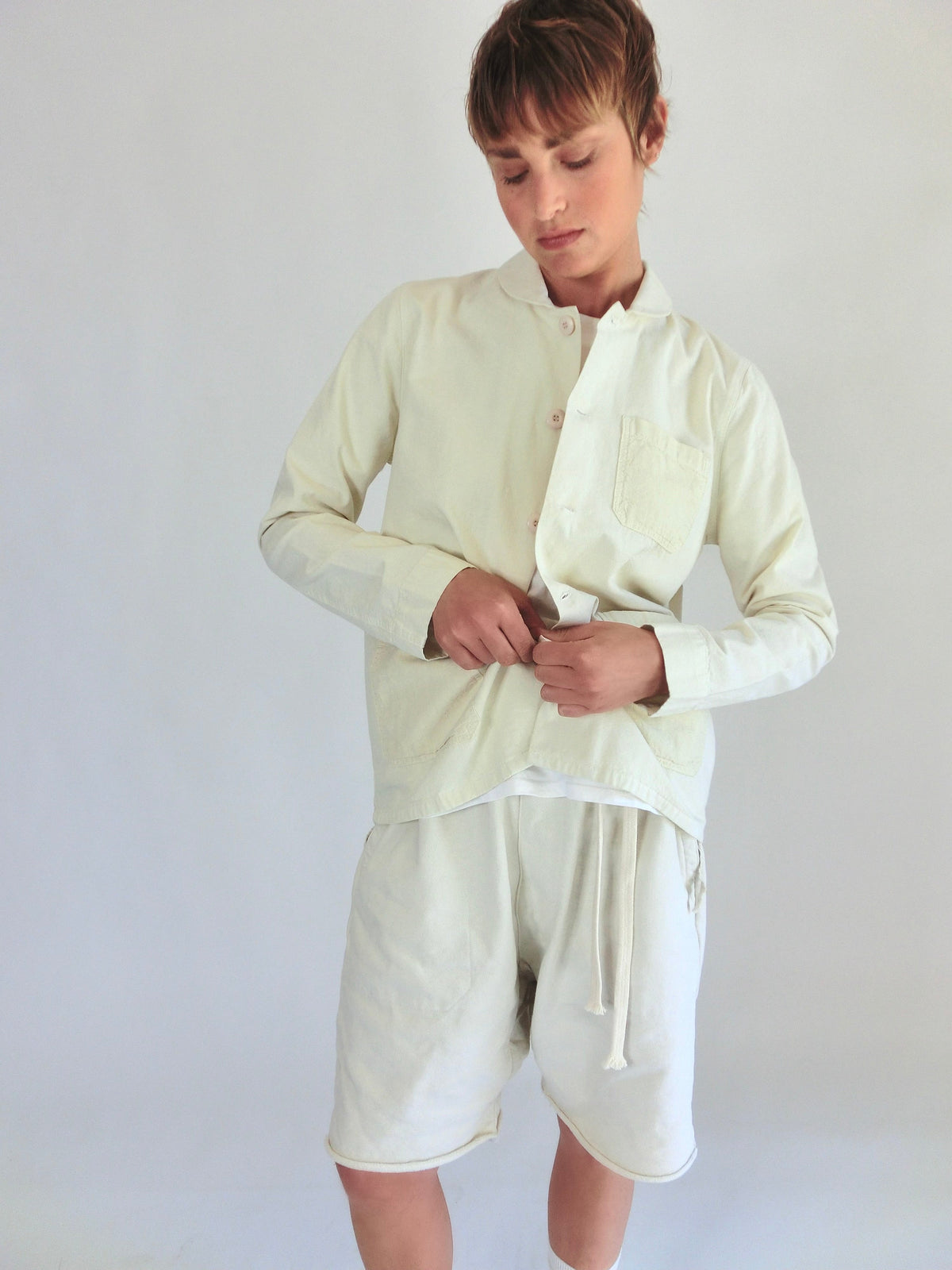 Model buttoning a cream Travelers Jacket over a white shirt with matching cream drawstring shorts.