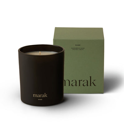 Black candle in a container with 'marak' branding next to a green box on a white background