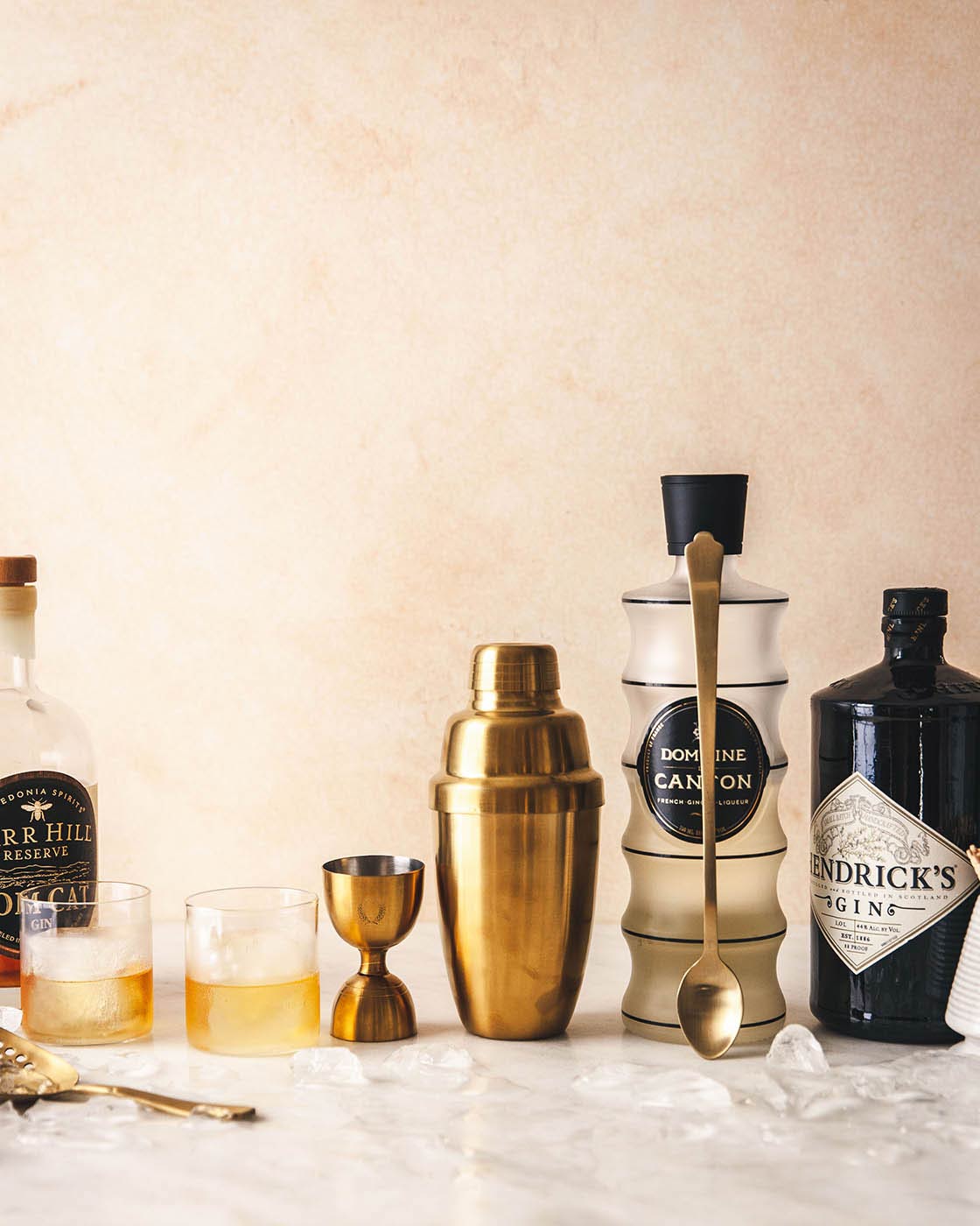 Complete gold barware set arranged with liquor bottles and prepared cocktails on a marble counter.