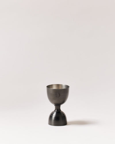 Double-sided brushed-onyx jigger standing upright with dark exterior cups and a contrasting silver interior.