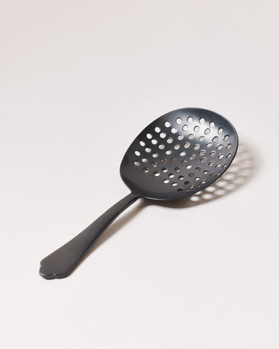 Brushed-onyx perforated cocktail strainer with a broad oval bowl, round drainage holes, and short decorative handle.