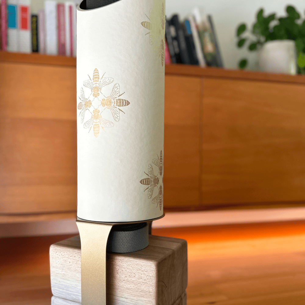 Close-up of the Apis tube and pale wood base in a warm interior, showing scattered metallic-gold bee motifs.