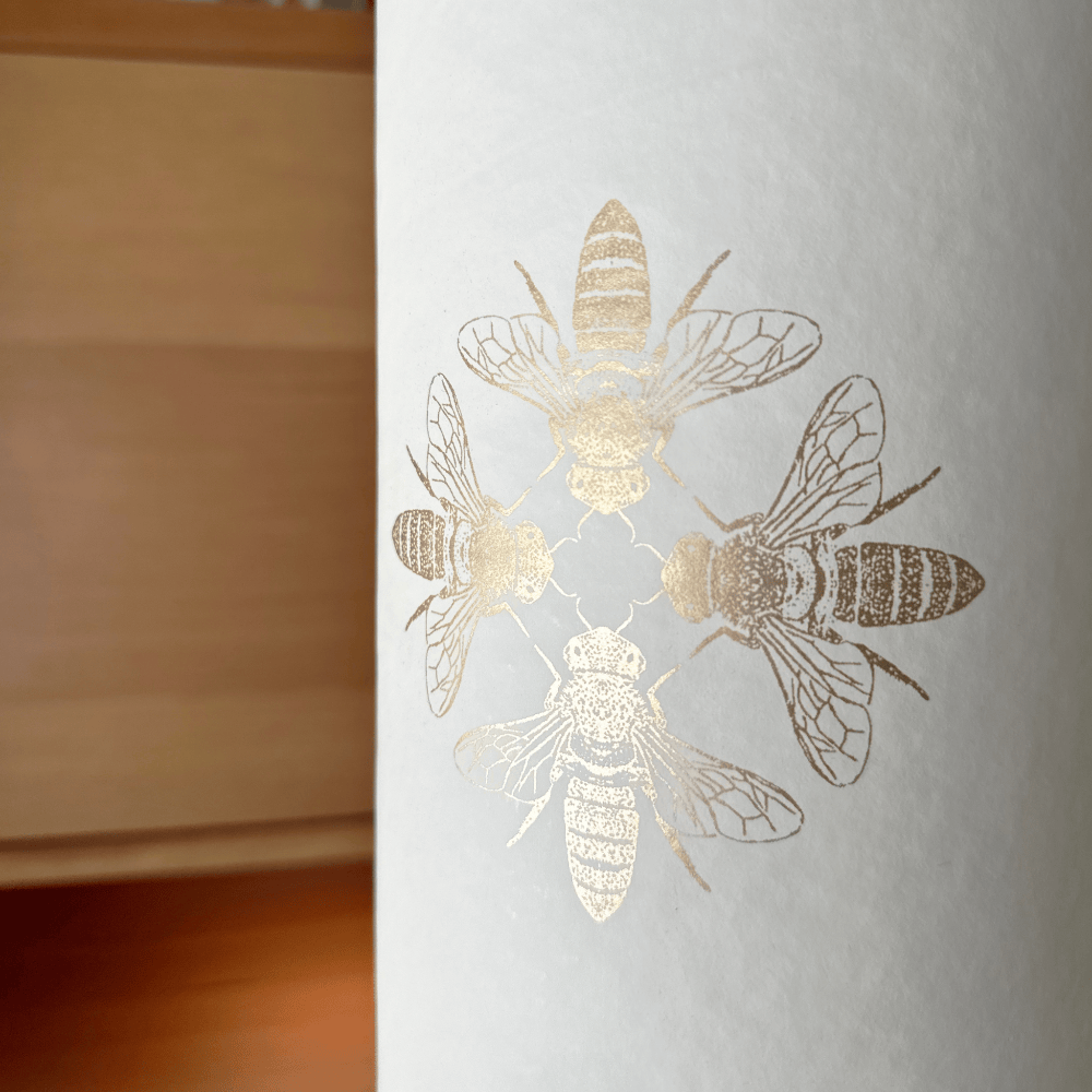 Detailed view of the central design featuring a cluster of finely drawn gold bees on the softly textured white surface.