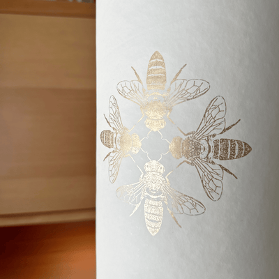 Detailed view of the central design featuring a cluster of finely drawn gold bees on the softly textured white surface.