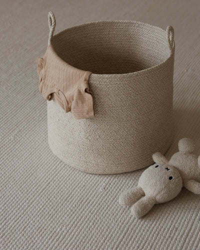 Tall rope basket holding a soft pink textile, styled beside a plush toy.