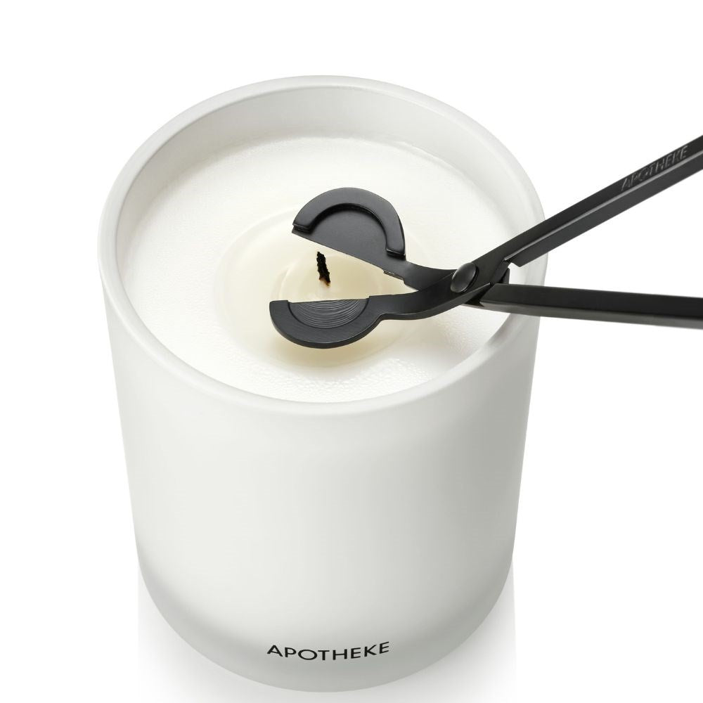 Black wick trimmer positioned around the wick of an unlit candle, viewed from above in a white vessel filled with white wax.