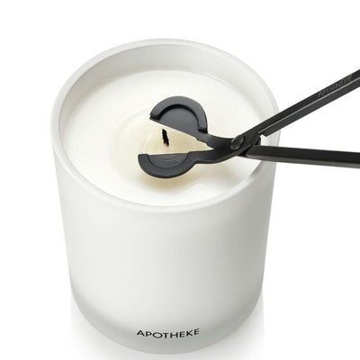Black wick trimmer positioned around the wick of an unlit candle, viewed from above in a white vessel filled with white wax.
