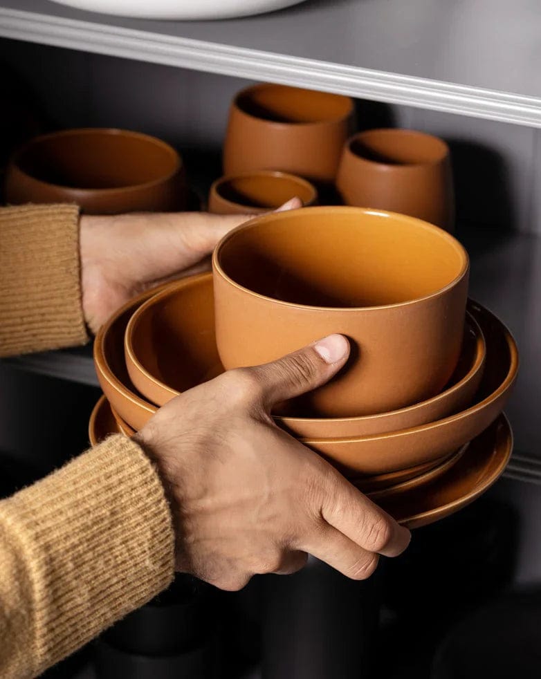 Person stacking stoneware bowls in Terracotta on kiln shelving during production