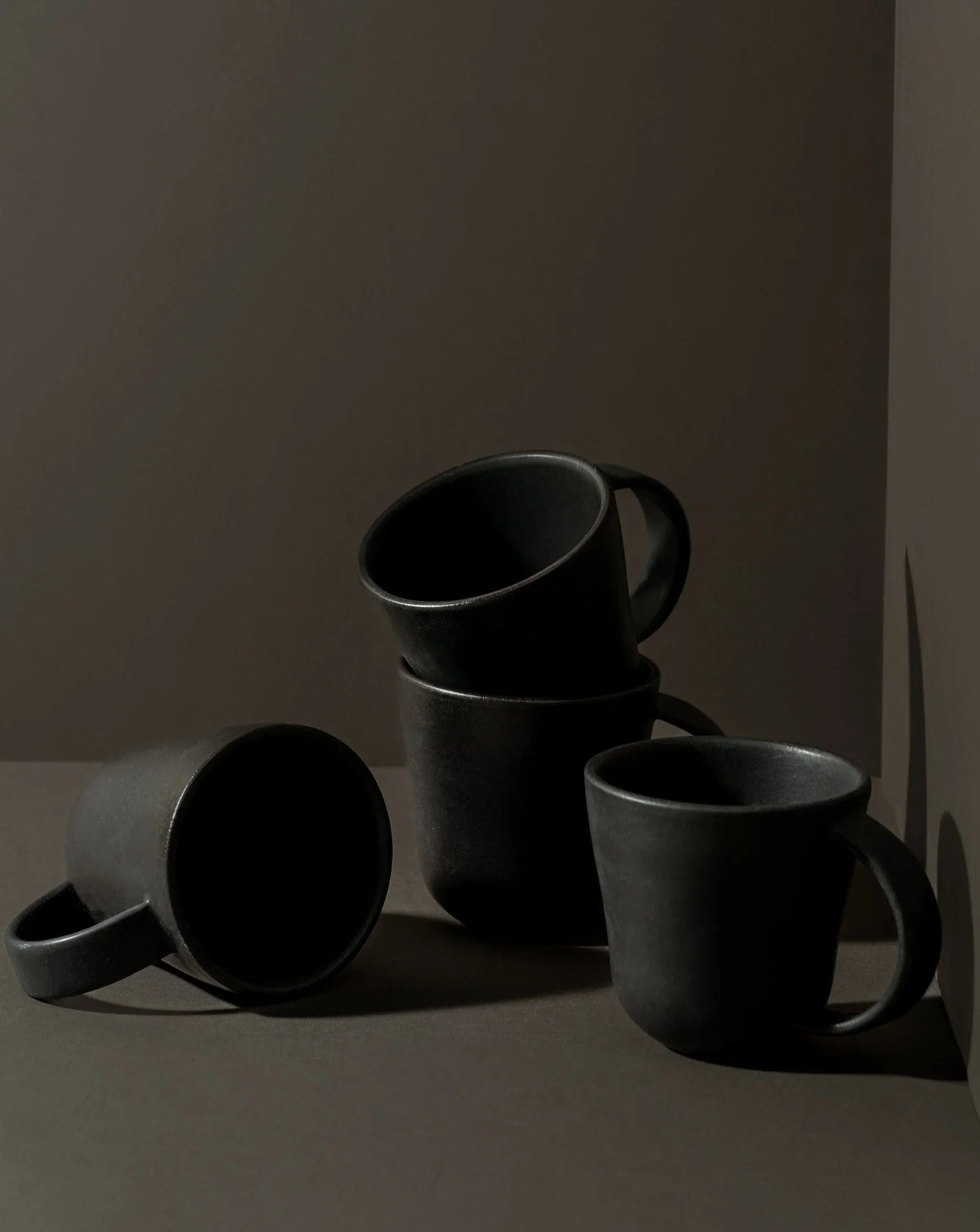 Stoneware mugs in Matte Black styled together on dark background