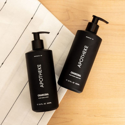 APOTHEKE Charcoal Lotion and Liquid Soap bottles paired together on a light wood surface