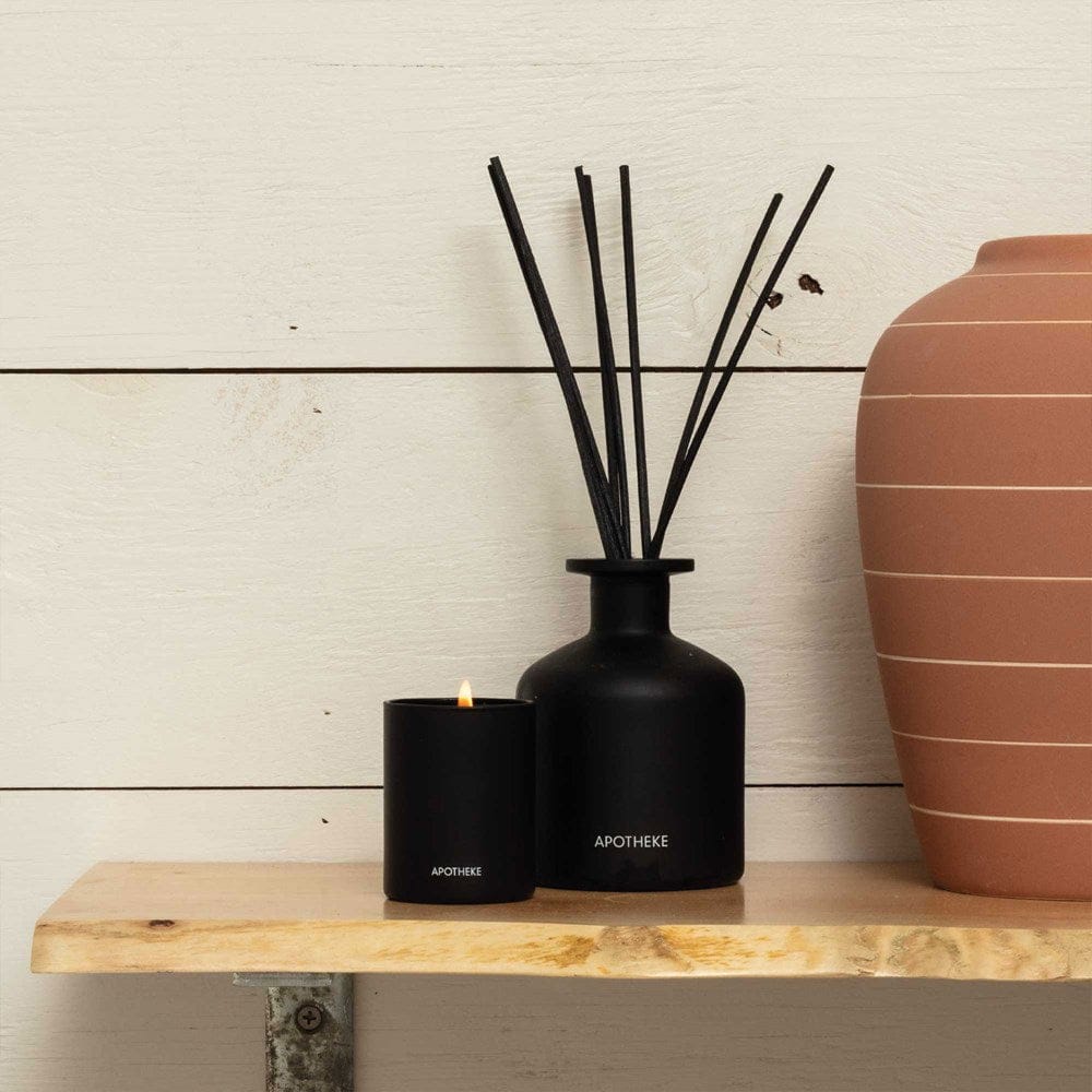 APOTHEKE Charcoal Reed Diffuser displayed on a wood shelf beside a matching votive candle and terracotta vase