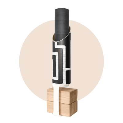 Black cylindrical yoga mat tube with a bold white maze pattern, holding a rolled black mat and standing on four pale wood blocks with a black support strap.
