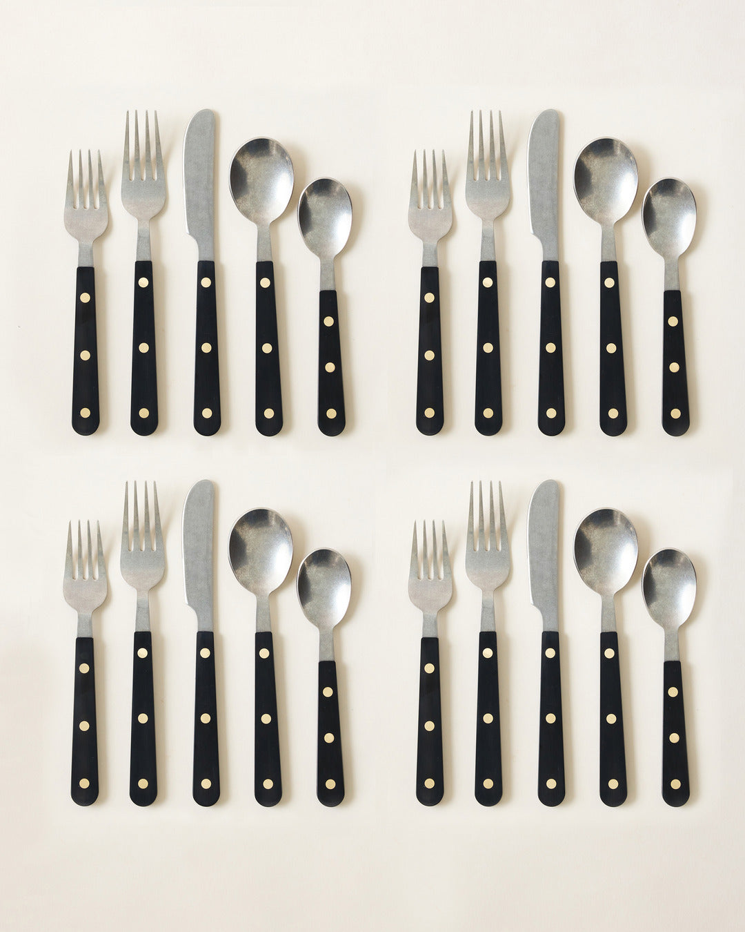 Two complete black-handled cutlery settings arranged in rows, with polished metal utensils and three bright rivets on each handle.