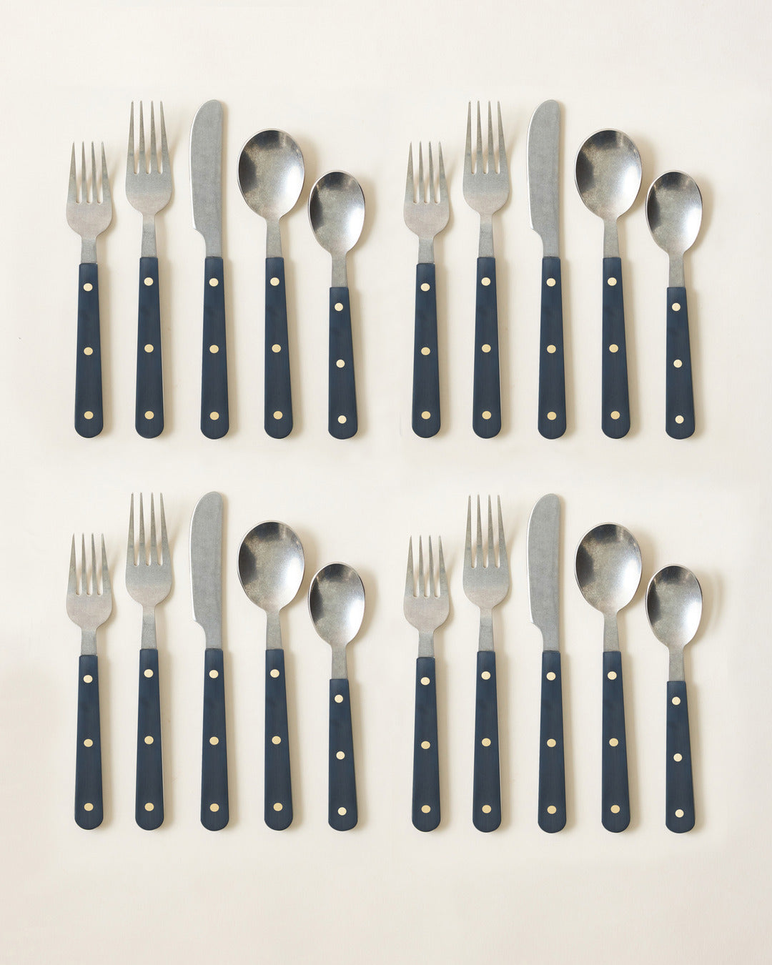 Two complete navy-handled cutlery settings with polished stainless-steel heads and contrasting brass-toned rivets.