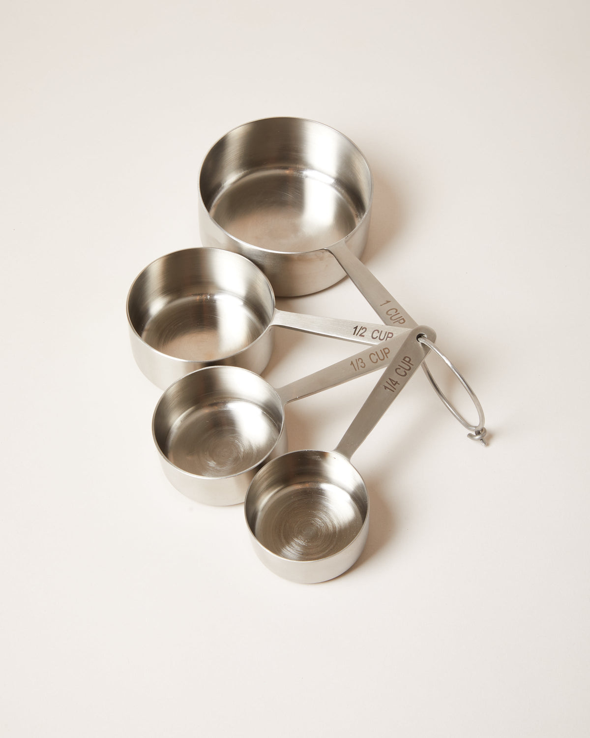 Four stainless steel measuring cups in graduated sizes, fanned outward and secured by a small metal ring.