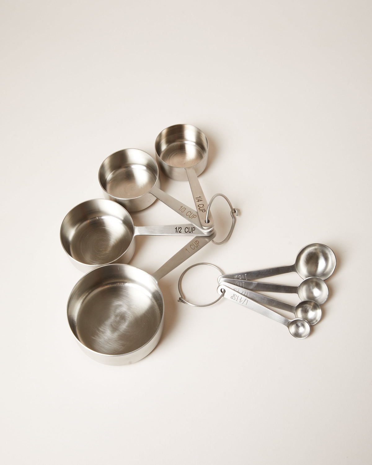 Coordinating stainless steel measuring cups and measuring spoons arranged side by side, each set held by a circular ring.