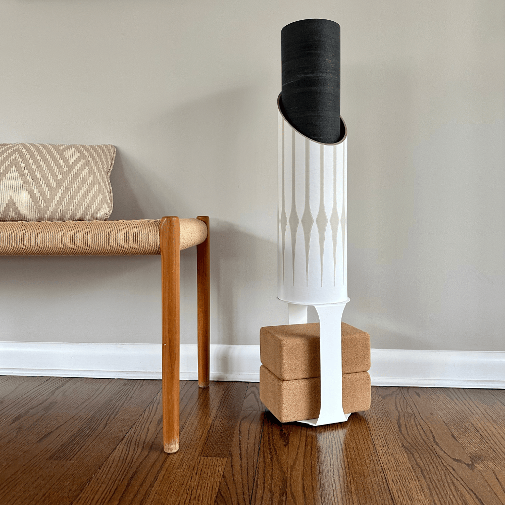 Gather tube displayed beside a woven bench on hardwood flooring, supported by natural wood blocks and a white strap.