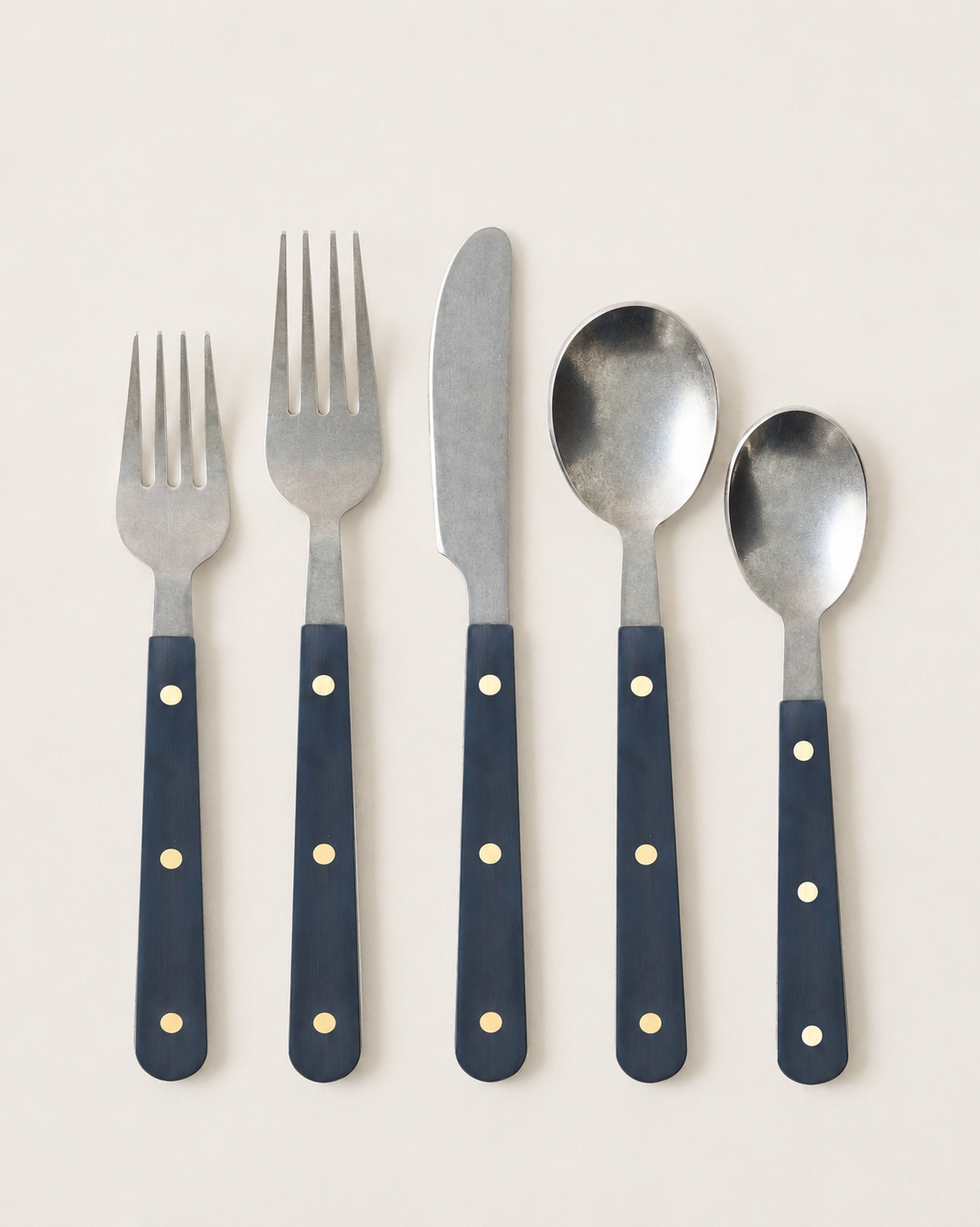 Close product view of a five-piece navy Heritage Cutlery setting with two forks, a knife, a tablespoon, and a teaspoon.
