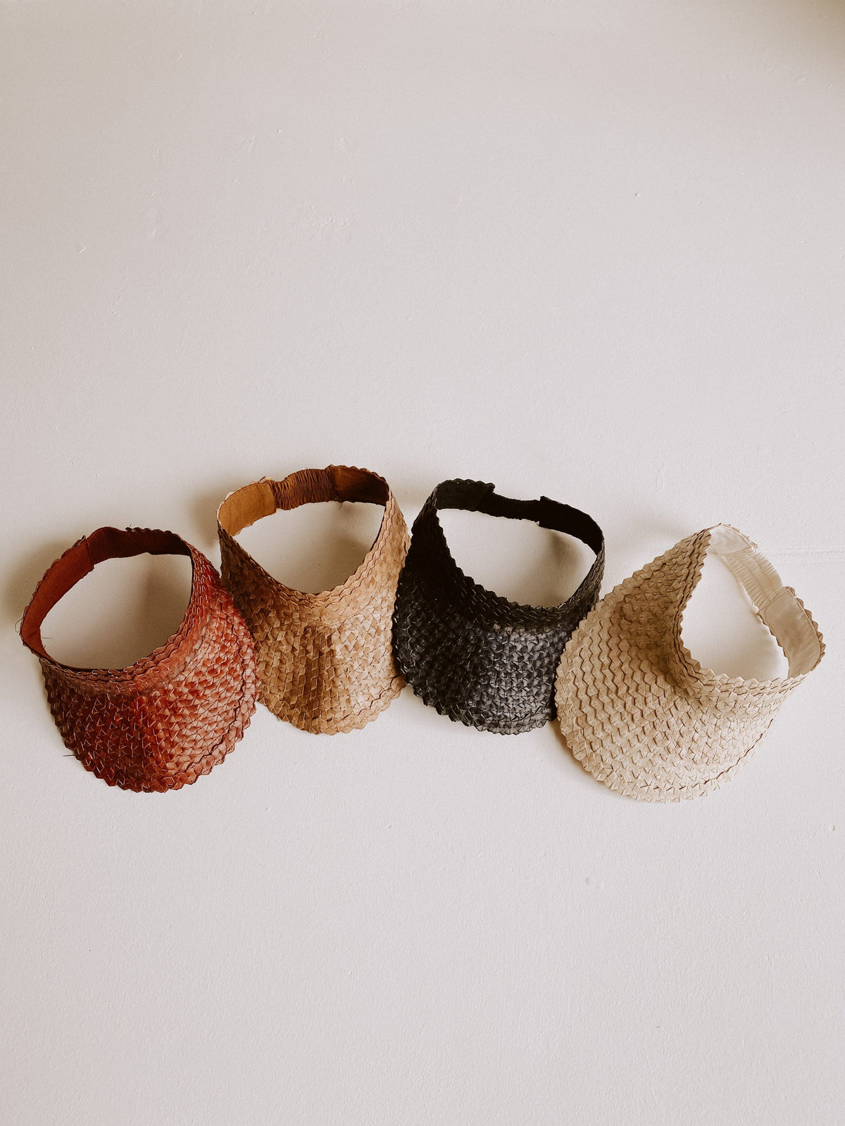 Village Thrive Rattan Sun Visors, clay, blonde, black, and amber palm leaf, four visors laid flat side by side.