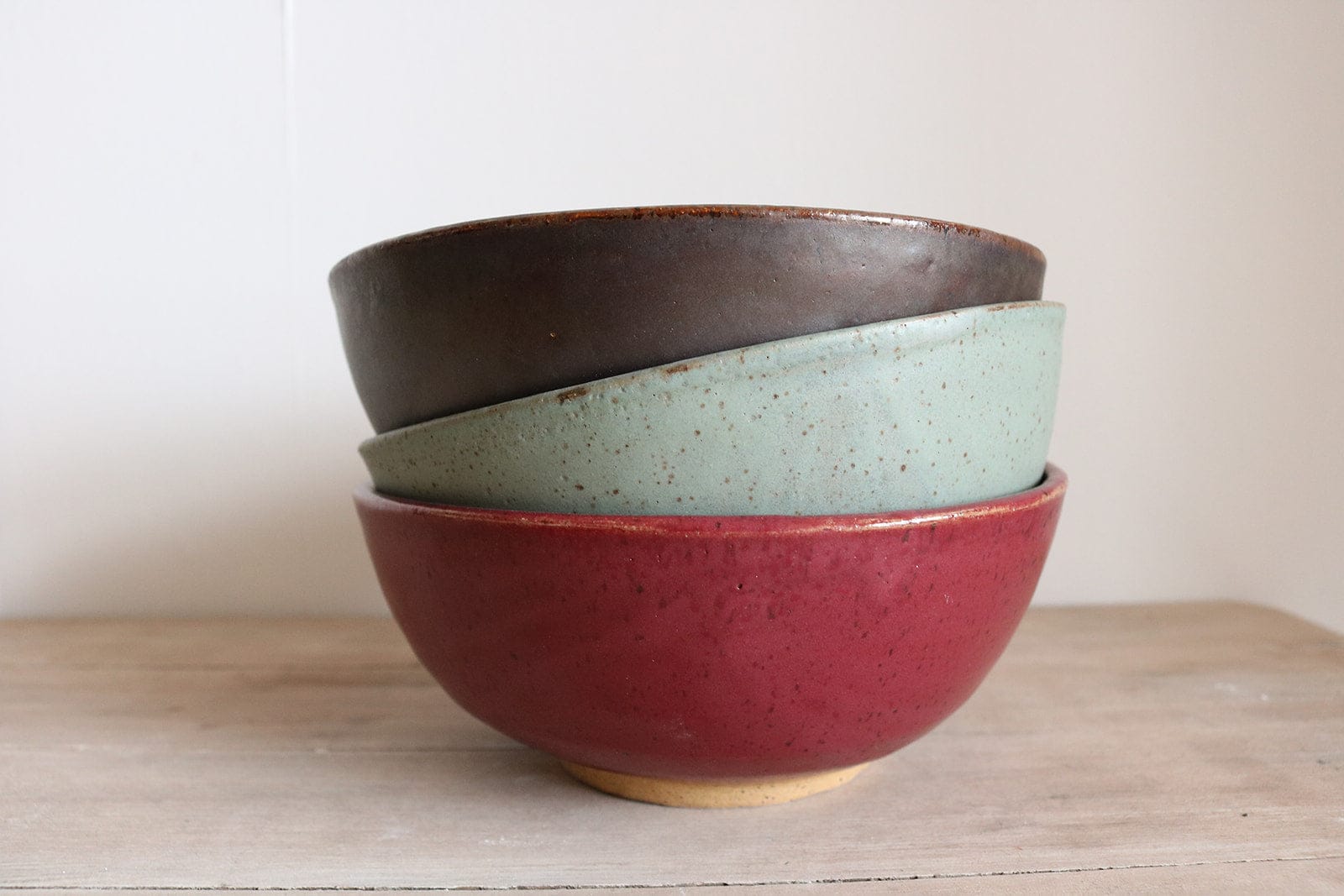 Three ceramic bowls stacked on a wooden surface with a white background
