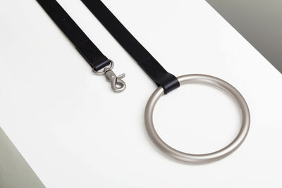 Limited-edition black Lumi Leash with a slim stitched strap, brushed-silver swivel clasp, and oversized circular metal handle.