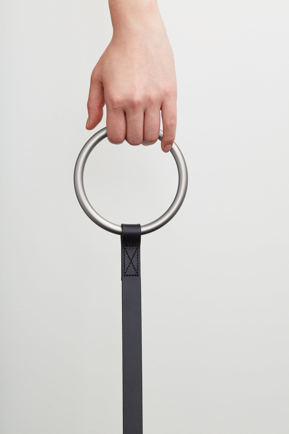 Hand gripping the oversized silver ring handle while the narrow black leash strap hangs vertically.