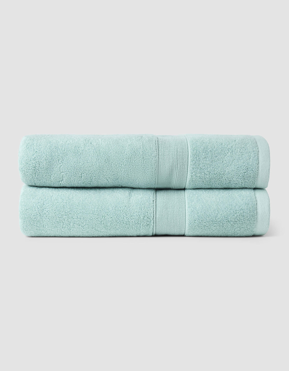 Two pale aqua bath towels folded and stacked on a light gray background, with woven border bands aligned near the right side.