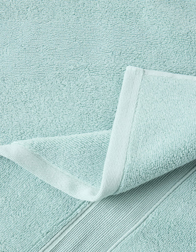 Close-up of a pale aqua towel with a corner folded back, revealing dense looped texture, a stitched edge, and a ribbed border.