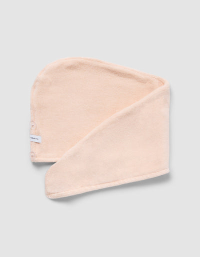 Pale peach hair towel displayed flat with an overlapping fold, showing its rounded shape, textured surface, and finished edge.