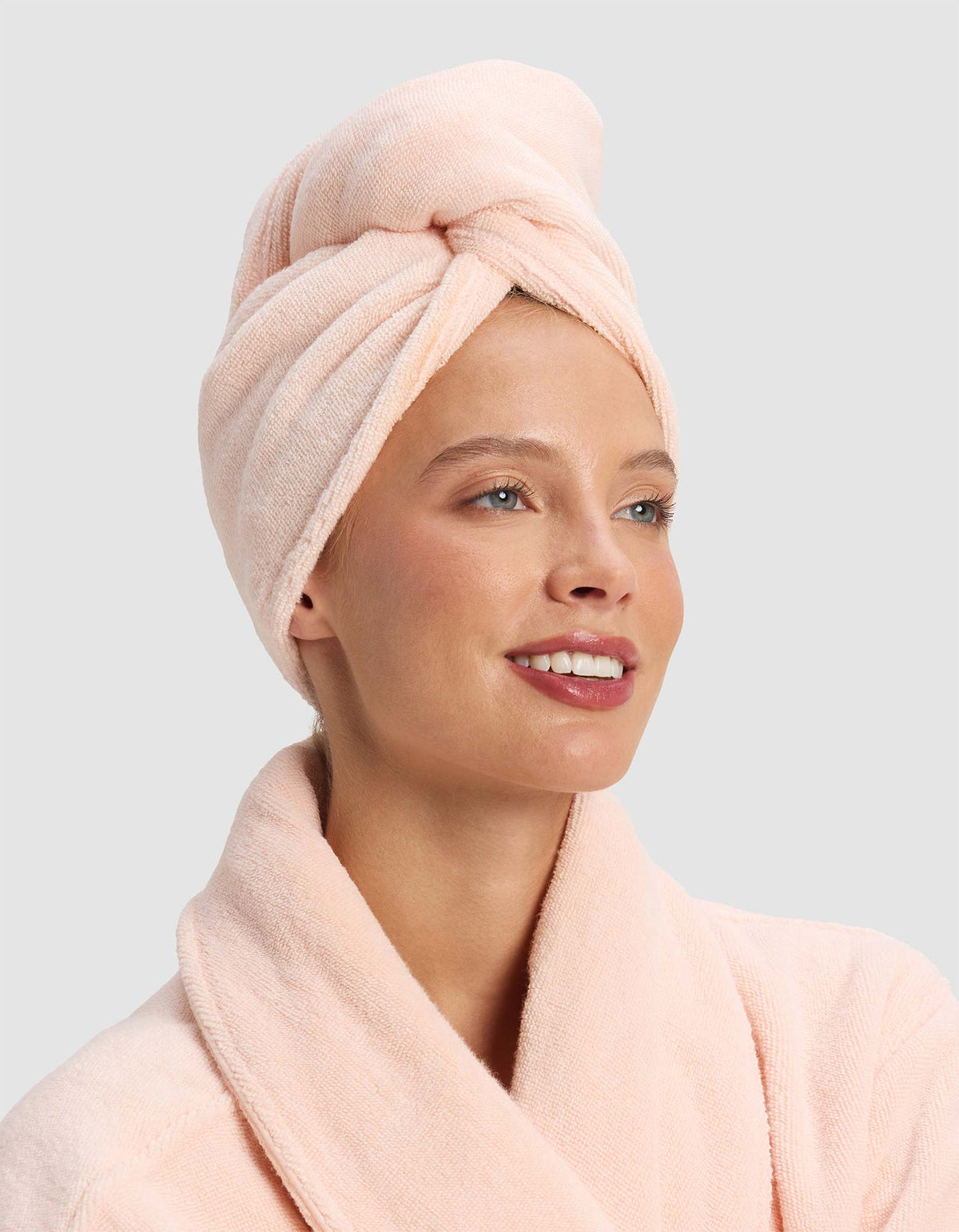 Model wearing a pale peach hair towel twisted above her forehead, paired with a matching plush robe.