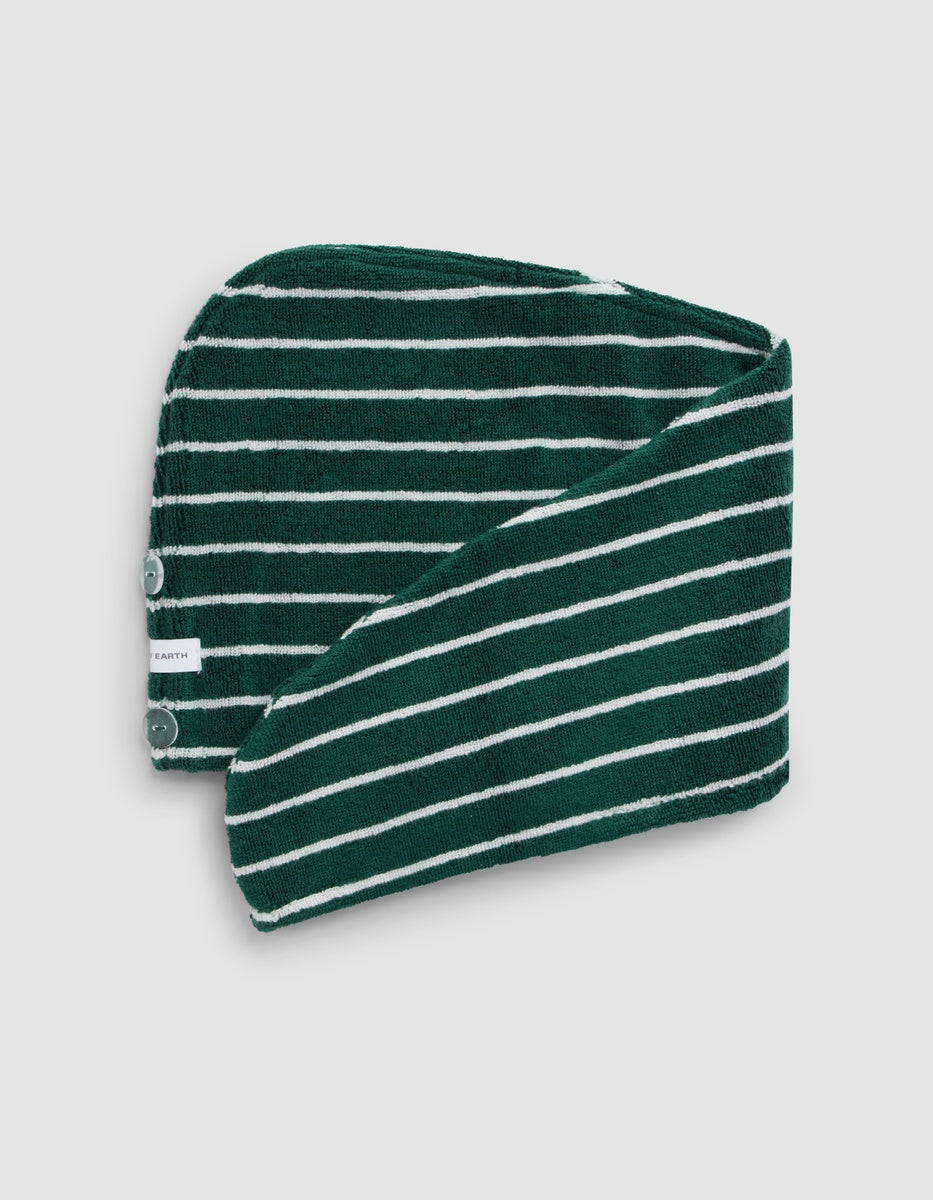 Deep green hair towel with narrow white stripes displayed flat with an overlapping fold, showing its curved edge, white button, and small fabric label.